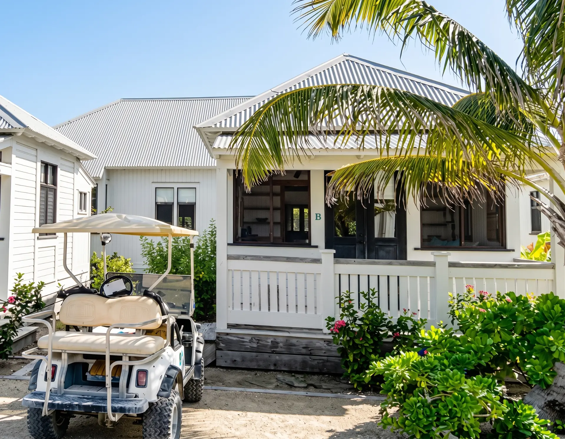Golf cart parked beside a white cottage porch under palms
